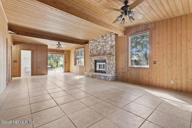 unfurnished living room featuring wood walls, a wealth of natural light, beamed ceiling, and a stone fireplace