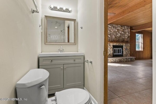 bathroom featuring wooden walls, toilet, wood ceiling, a stone fireplace, and vanity