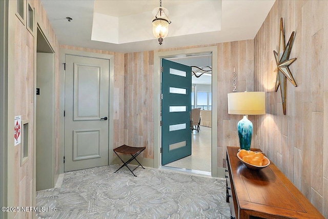 foyer with a tray ceiling, visible vents, and wooden walls