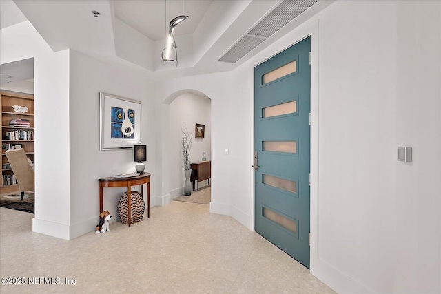 foyer featuring baseboards, arched walkways, and a tray ceiling