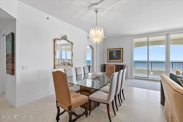 dining space with arched walkways, a water view, a wall of windows, a chandelier, and baseboards