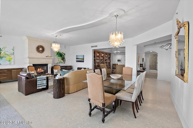 dining space with arched walkways, visible vents, a chandelier, a warm lit fireplace, and baseboards