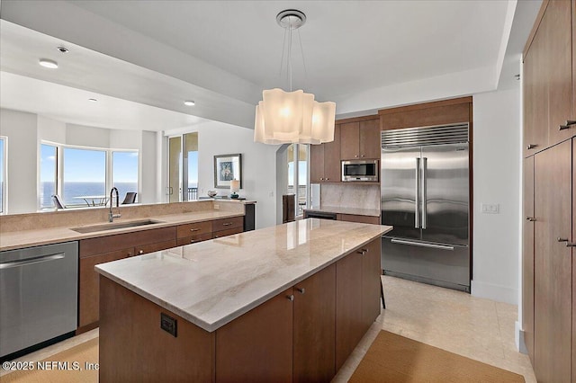 kitchen featuring a kitchen island, light stone counters, appliances with stainless steel finishes, pendant lighting, and a sink