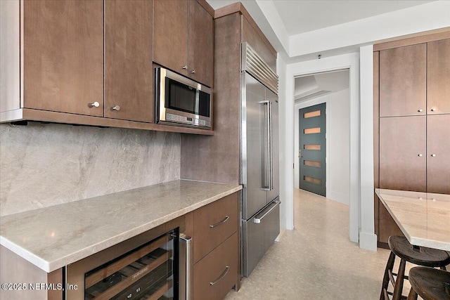 kitchen featuring beverage cooler, decorative backsplash, appliances with stainless steel finishes, light stone counters, and light floors