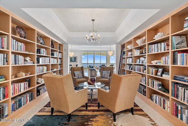 living area with a tray ceiling, bookshelves, and an inviting chandelier