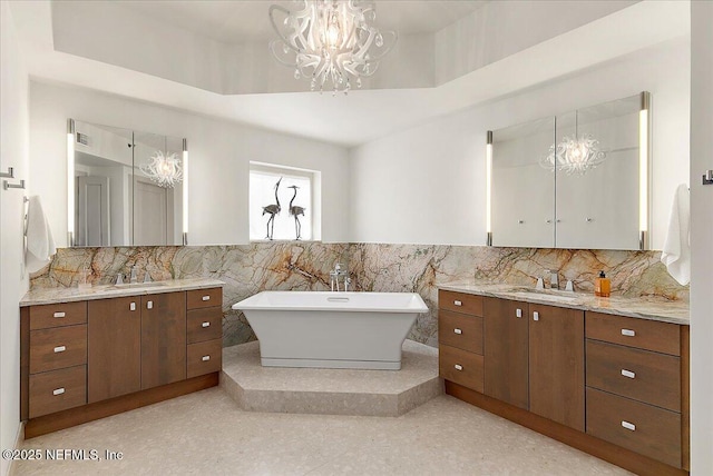 full bath featuring a freestanding tub, two vanities, a raised ceiling, and a sink