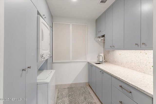 laundry area with a sink, stacked washer and dryer, visible vents, and cabinet space