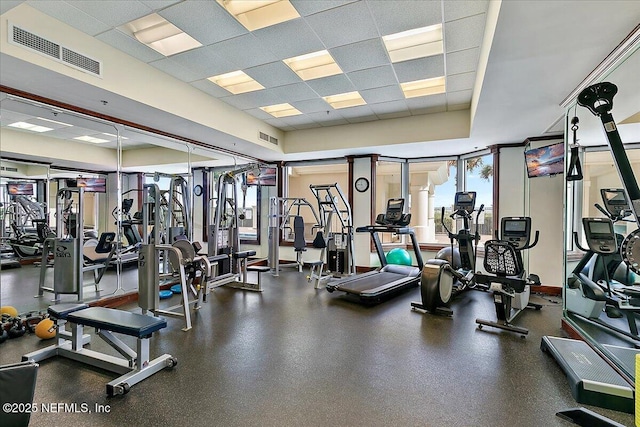 exercise room with a wealth of natural light, visible vents, a drop ceiling, and a tray ceiling