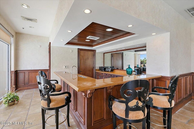 bar featuring a wainscoted wall, visible vents, a raised ceiling, and a sink