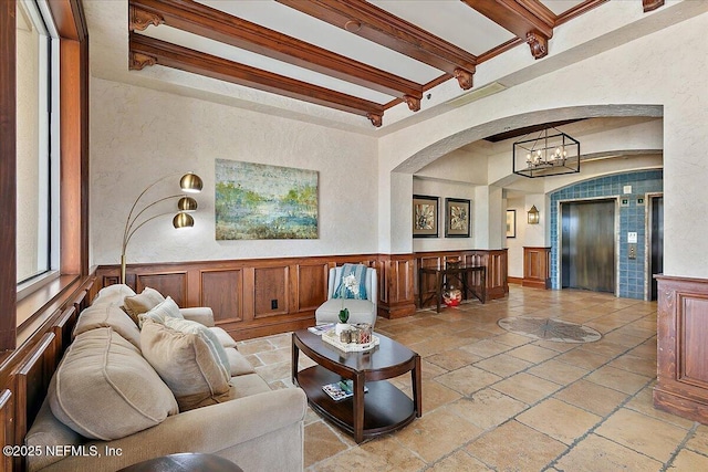 living room with beam ceiling, wainscoting, elevator, and stone tile floors