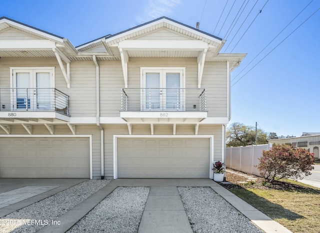 view of front of house featuring an attached garage, a balcony, fence, concrete driveway, and french doors