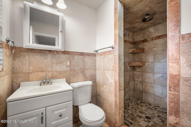 full bathroom with a wainscoted wall, tile walls, toilet, vanity, and tiled shower