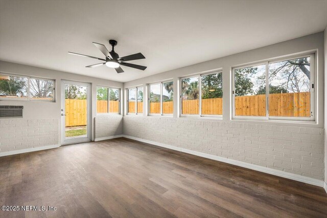 unfurnished sunroom with plenty of natural light, a ceiling fan, and an AC wall unit