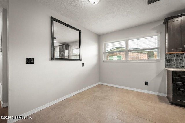 unfurnished dining area featuring a textured ceiling and baseboards