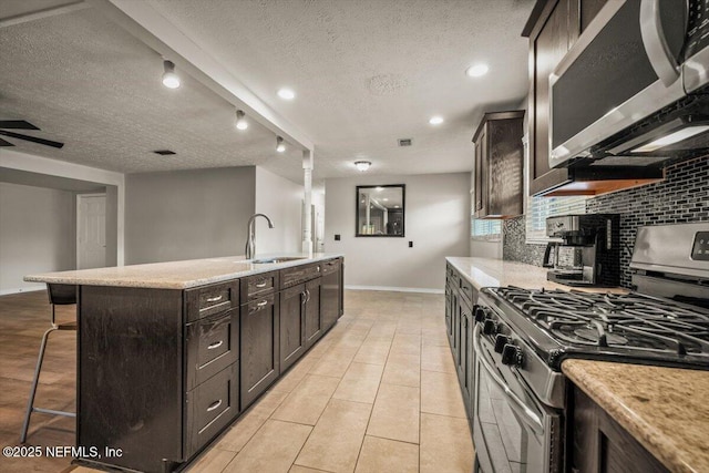 kitchen featuring decorative backsplash, appliances with stainless steel finishes, a breakfast bar, a textured ceiling, and a sink