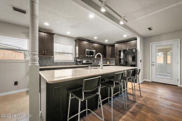 kitchen featuring a spacious island, stainless steel microwave, backsplash, a sink, and dark brown cabinets