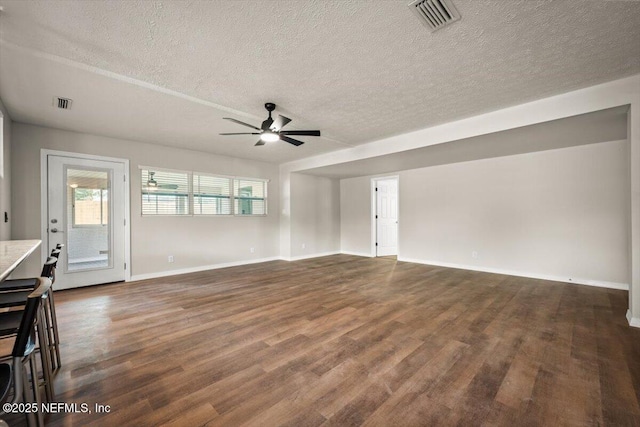 unfurnished living room featuring dark wood-style flooring, visible vents, and baseboards