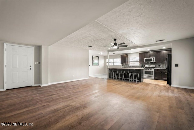 unfurnished living room with ceiling fan, light wood-style flooring, baseboards, and a textured ceiling