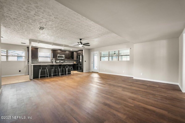 unfurnished living room with a ceiling fan, baseboards, visible vents, and wood finished floors