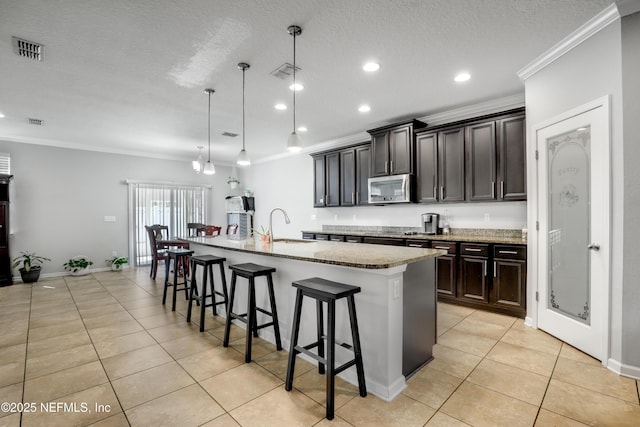 kitchen featuring visible vents, a sink, stainless steel microwave, crown molding, and light tile patterned floors