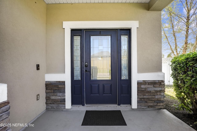 view of exterior entry featuring stucco siding, stone siding, and fence