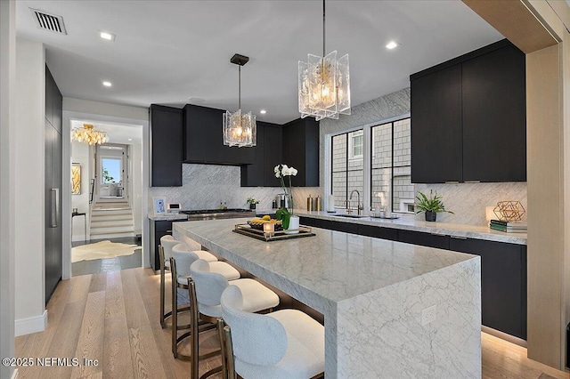 kitchen with a kitchen island, a sink, visible vents, and dark cabinets