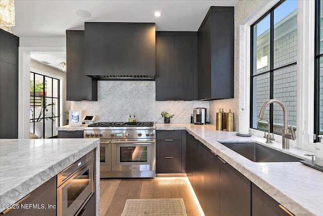 kitchen featuring range with two ovens, a sink, light wood-type flooring, tasteful backsplash, and custom range hood