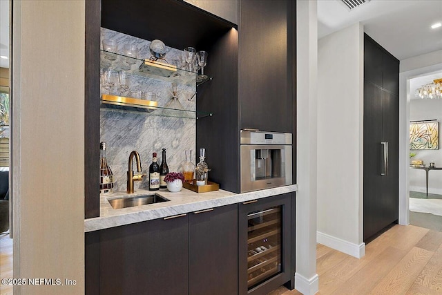 bar with light wood-style floors, stainless steel oven, a sink, wet bar, and beverage cooler