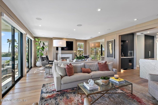 living area featuring beverage cooler, a lit fireplace, light wood finished floors, and recessed lighting