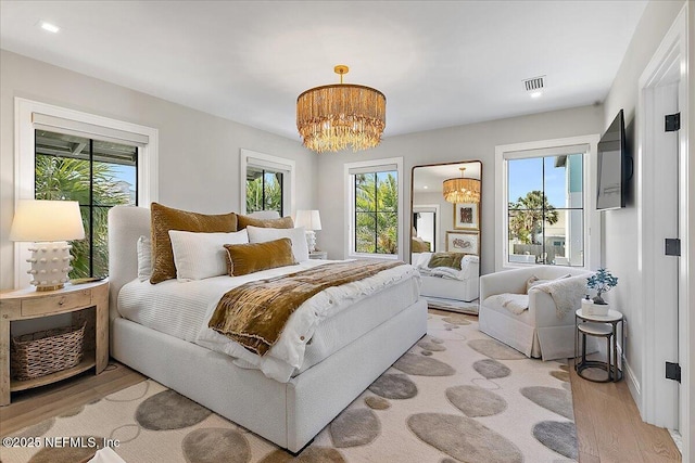 bedroom featuring light wood-type flooring, visible vents, multiple windows, and an inviting chandelier