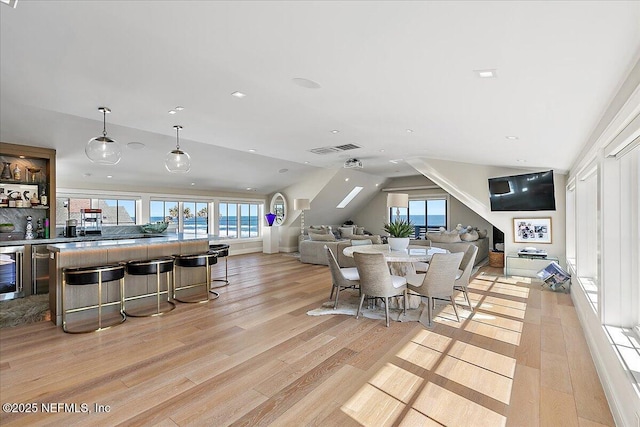 dining area with light wood-style floors, wine cooler, visible vents, and lofted ceiling