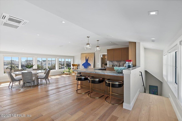 kitchen featuring brown cabinets, light wood finished floors, visible vents, plenty of natural light, and a kitchen breakfast bar