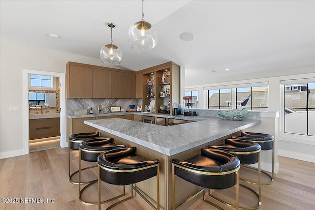 kitchen with a peninsula, light wood finished floors, tasteful backsplash, and a kitchen bar