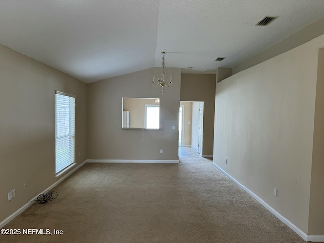 carpeted empty room with an inviting chandelier, baseboards, visible vents, and vaulted ceiling