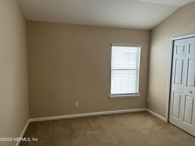 spare room featuring light carpet, a textured ceiling, and baseboards