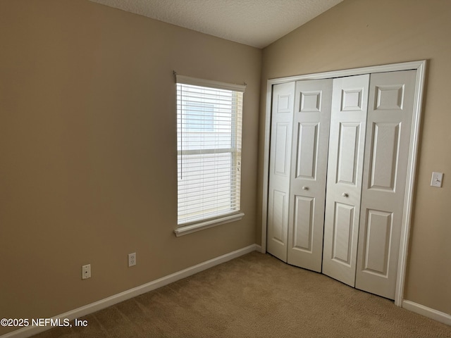 unfurnished bedroom with lofted ceiling, a textured ceiling, light colored carpet, baseboards, and a closet