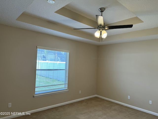 carpeted empty room with a ceiling fan, baseboards, a raised ceiling, and a textured ceiling