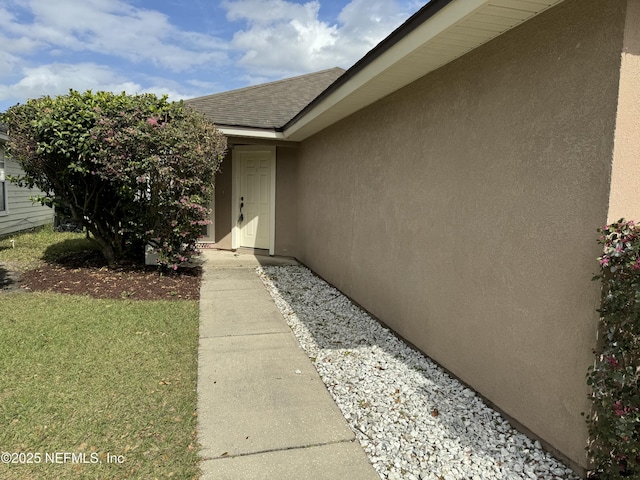 property entrance with a shingled roof and stucco siding