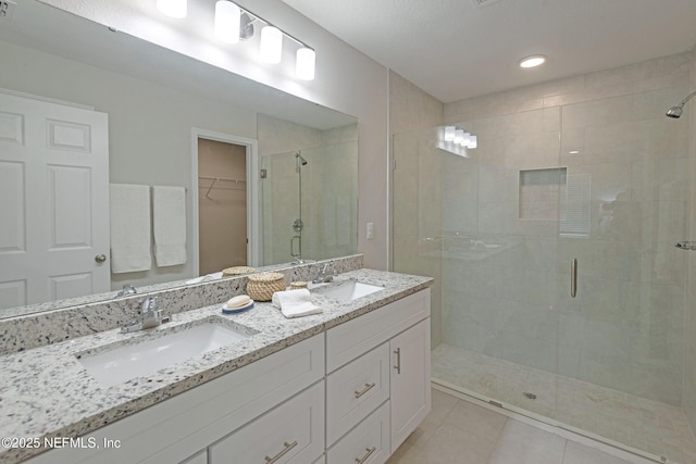 full bathroom with a spacious closet, double vanity, a sink, and a shower stall