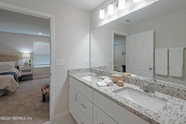 bathroom with ensuite bathroom, double vanity, a sink, and baseboards