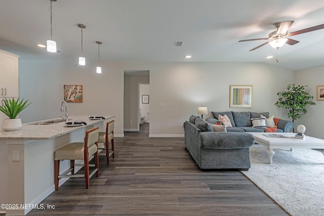 living area with dark wood-style flooring, visible vents, ceiling fan, and baseboards