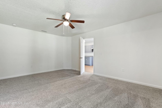 empty room with light carpet, visible vents, baseboards, a ceiling fan, and a textured ceiling