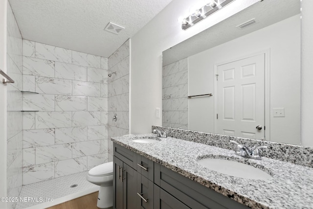 bathroom with a tile shower, a sink, and toilet