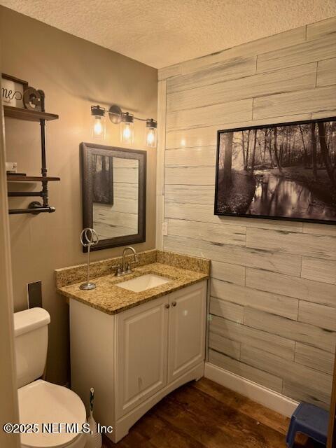 bathroom featuring toilet, wood walls, a textured ceiling, vanity, and wood finished floors