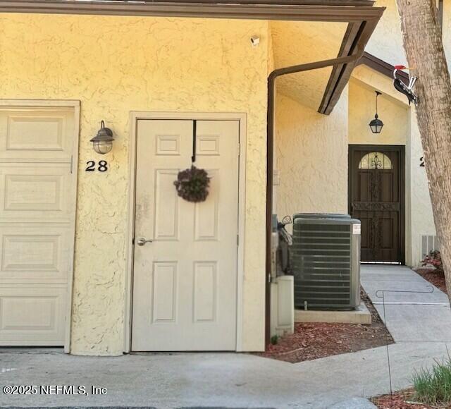 property entrance with central air condition unit, a garage, and stucco siding