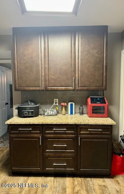 kitchen featuring light wood-style floors, dark brown cabinetry, decorative backsplash, and light stone countertops