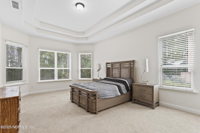 bedroom featuring light carpet, visible vents, multiple windows, and a tray ceiling