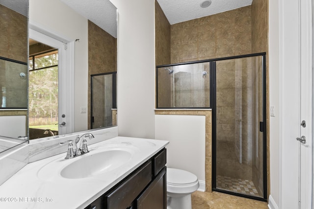 bathroom with toilet, a tile shower, a textured ceiling, vanity, and tile patterned flooring