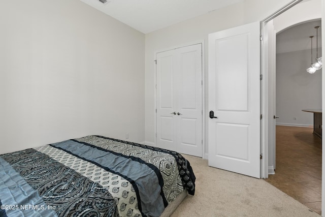 bedroom featuring arched walkways, a closet, light carpet, and baseboards