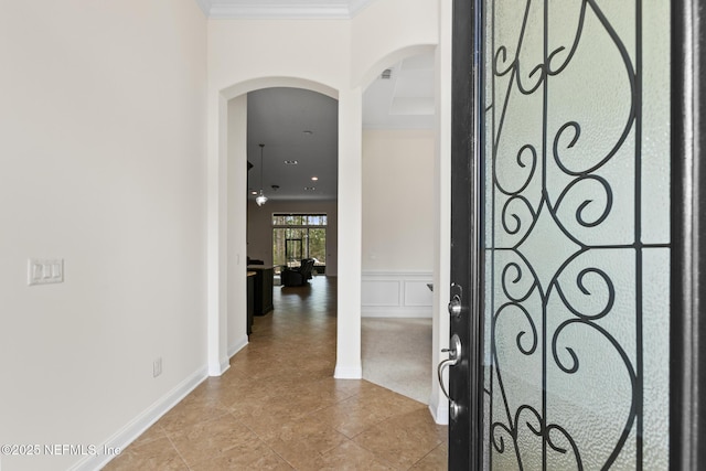 foyer entrance featuring arched walkways, wainscoting, ornamental molding, a decorative wall, and light tile patterned flooring